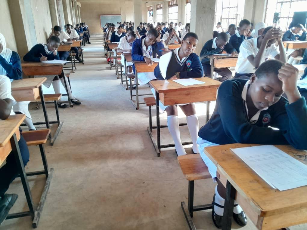 Students in school uniform writing an examination at individual desks in a Buloba Christian High School examination hall