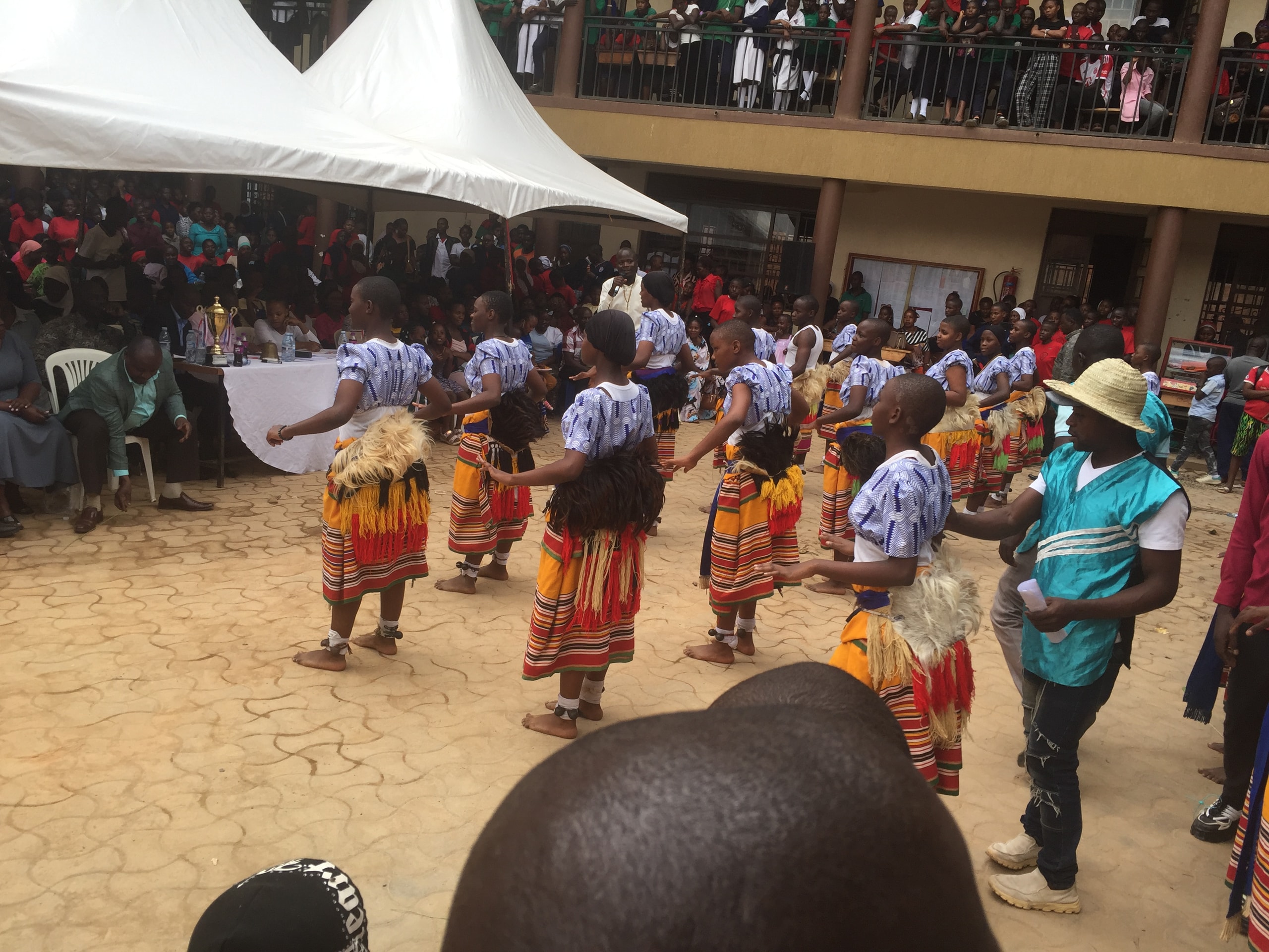 Students performing a traditional Ugandan dance in the school courtyard while the school watches from the balconies